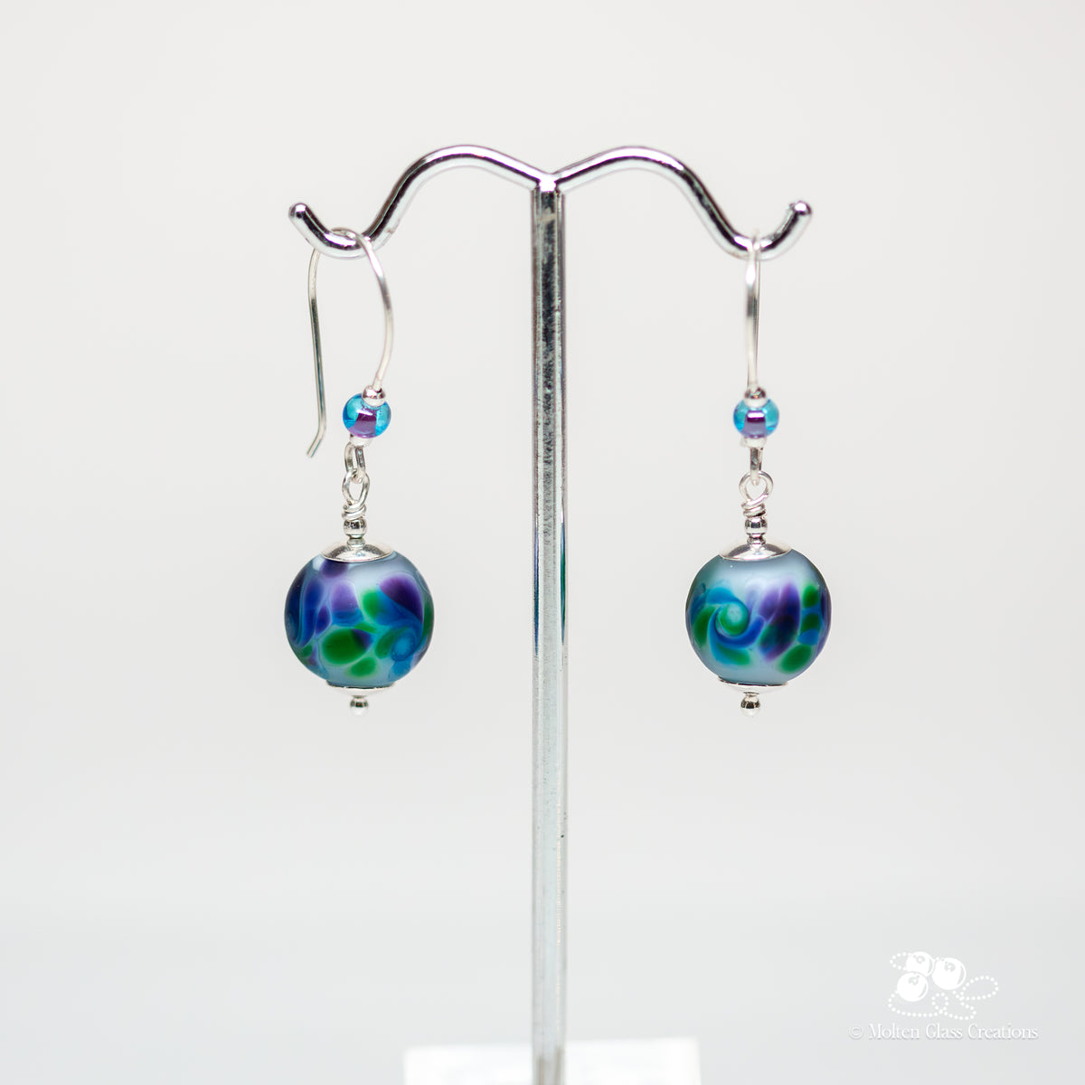 Lavender Frost Earrings - front view on display stand showing frosted lavender lampwork glass beads with purple and green crushed glass swirls