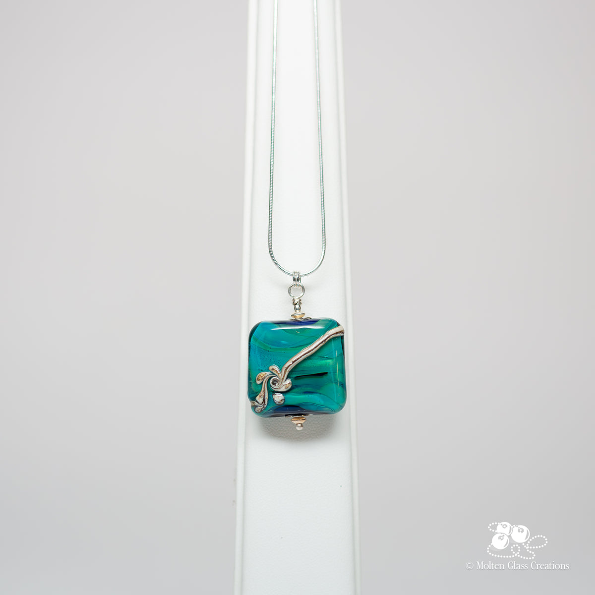 Teal Flourish Square Pendant - front view showing deep teal lampwork glass square bead with fine silver wire flourish on sterling silver snake chain